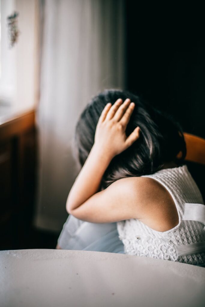 Young girl in emotional distress, sitting indoors with hand on head.